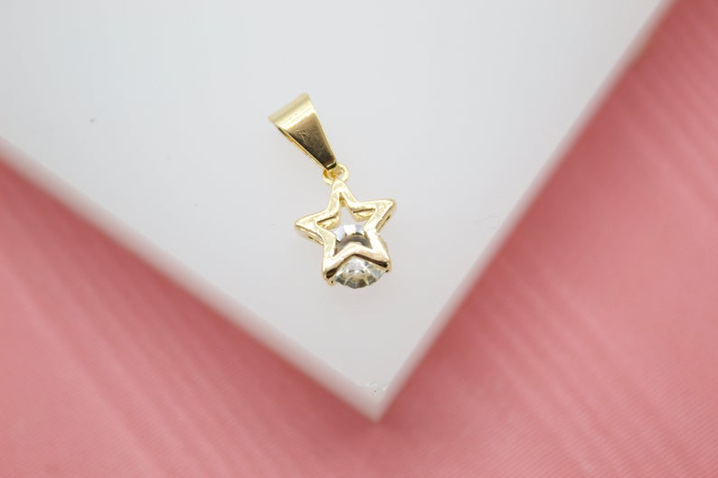 A sparkling diamond sparkles within a delicate gold star pendant resting on a white surface.
