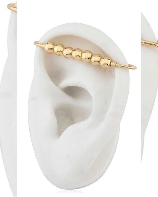 A gold industrial barbell earring featuring a row of smooth metal beads is showcased on a white model ear.