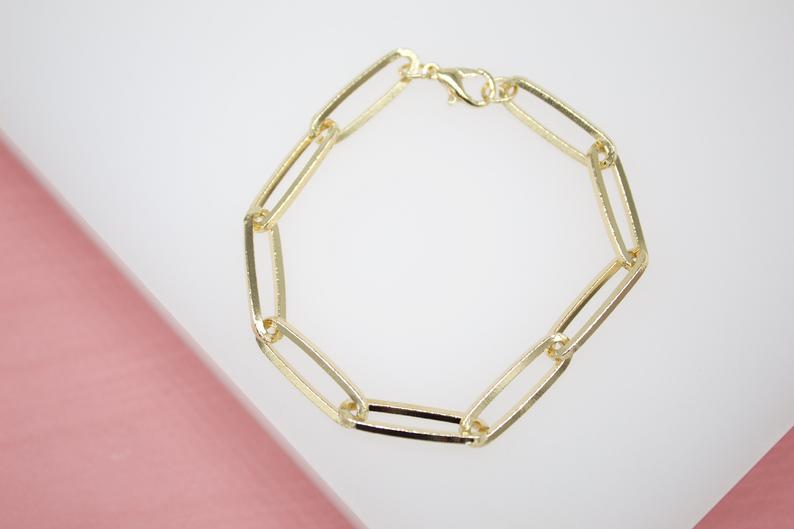 A gold paperclip chain bracelet rests on a white and pink surface.