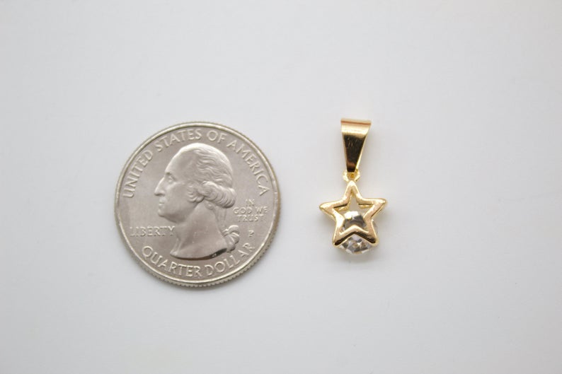 A gold star pendant with a sparkling crystal sits next to a US quarter coin for scale on a light surface.