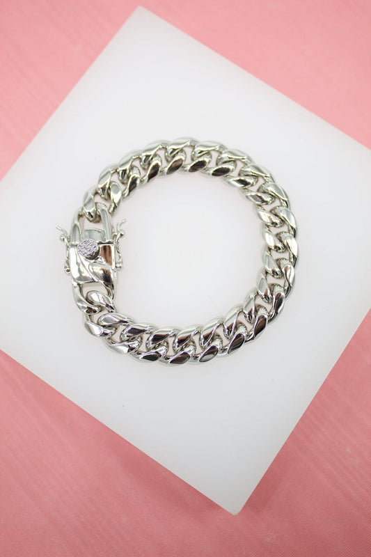 A polished silver cuban link bracelet rests neatly on a white display stand against a soft pink background.