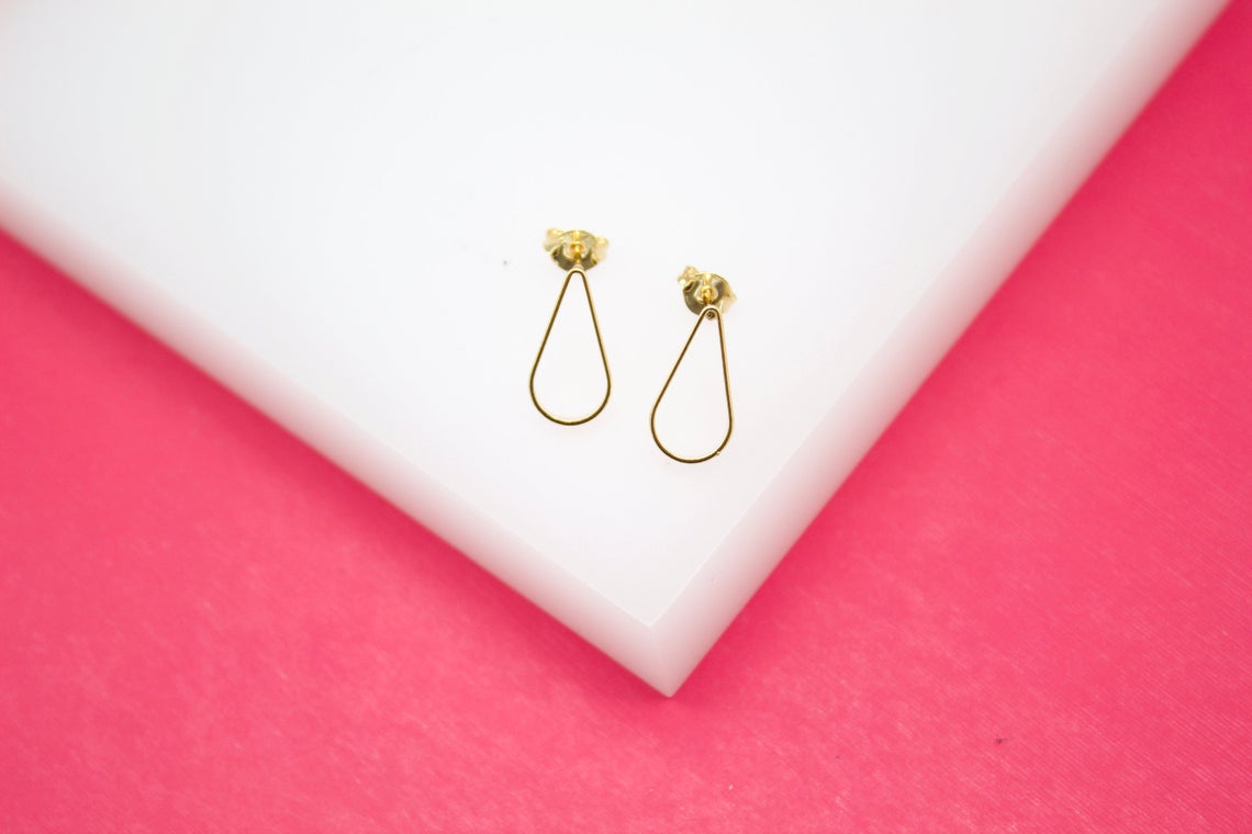 A pair of delicate gold teardrop stud earrings rests neatly on a white surface against a vibrant pink background.