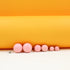 A row of six graduated pink ball stud earrings rests on a white surface against an orange backdrop.