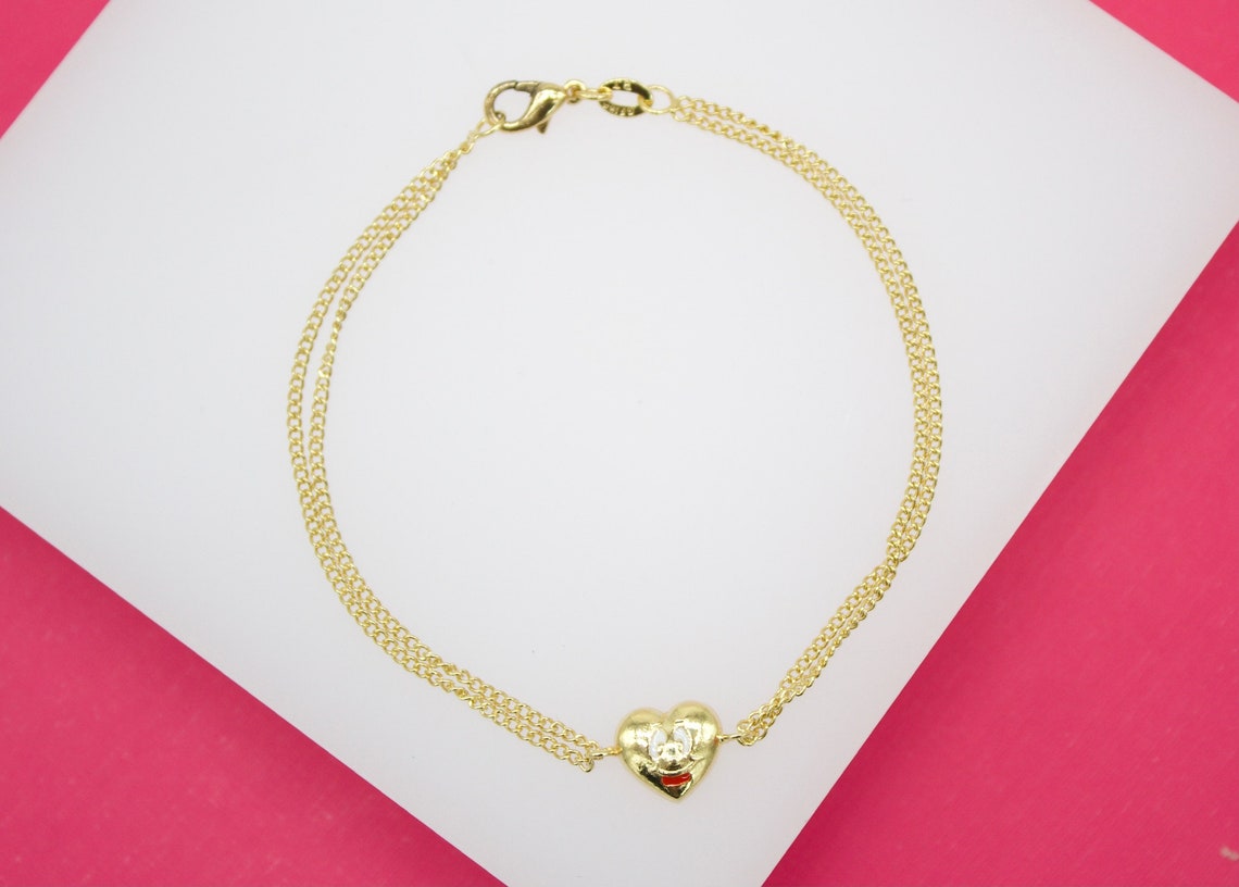 A gold double-strand bracelet features a heart-shaped charm with a cute cartoon face.