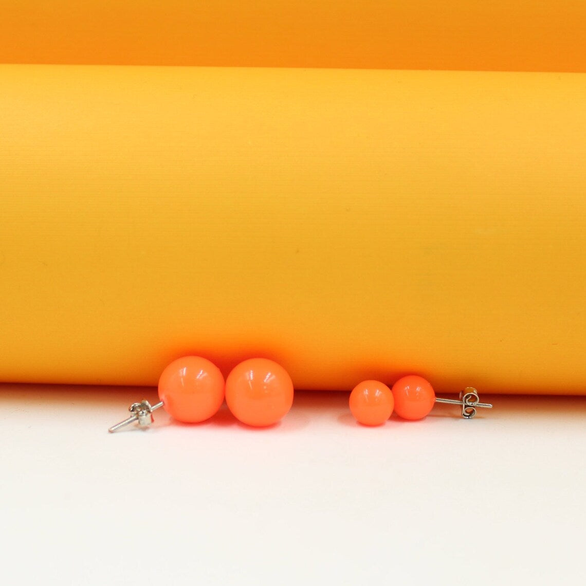 Bright orange ball stud earrings rest on a white surface against a vibrant yellow background.