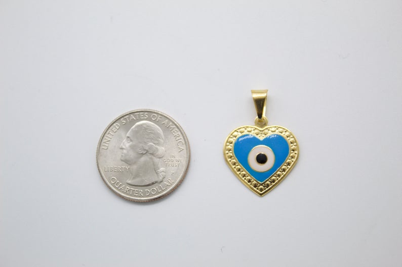 A gold heart-shaped evil eye pendant rests next to a US quarter coin to show its scale.