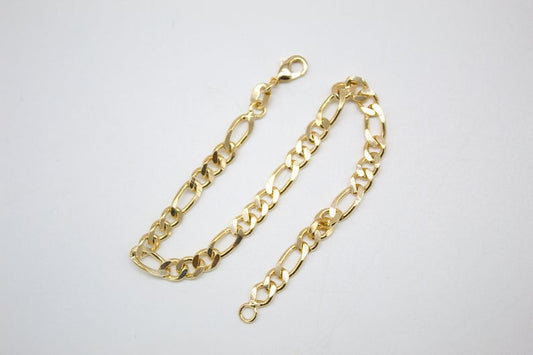 A polished gold Figaro link bracelet rests on a clean white surface, showcasing its classic alternating pattern.