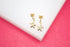 A pair of gold starfish earrings with sparkling diamond studs rest on a white surface against a bright pink background.