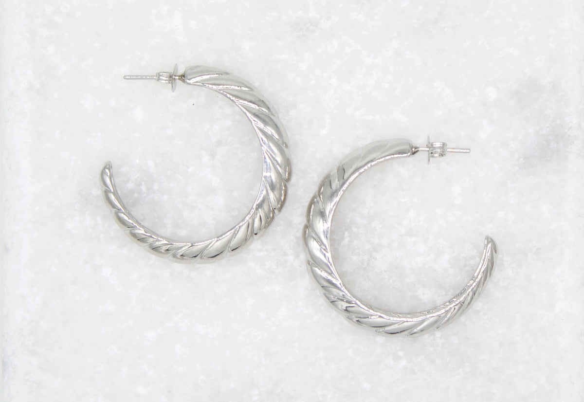 Two silver twisted hoop earrings rest on a textured white marble surface.