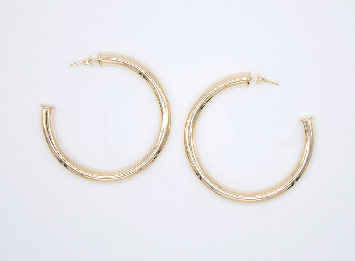 A pair of thick gold hoop earrings rests side-by-side against a plain white background.