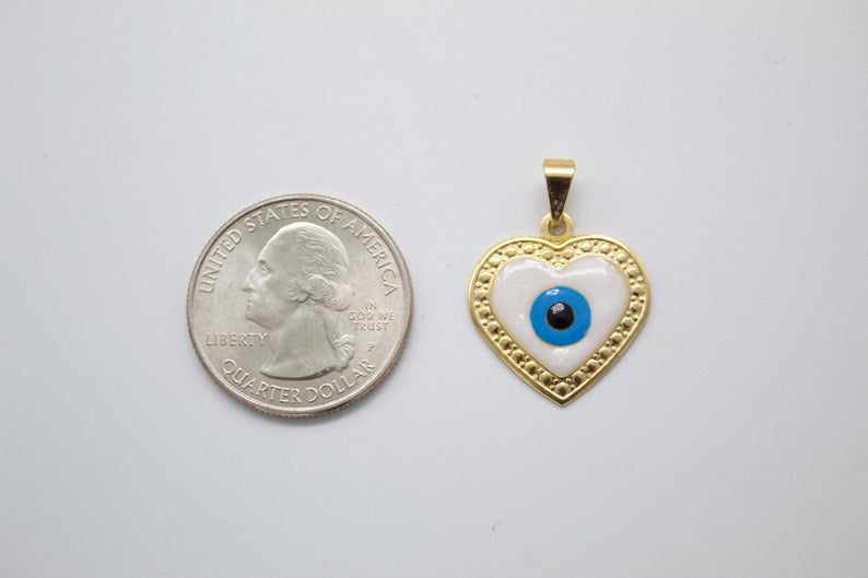 A gold heart-shaped evil eye pendant rests next to a US quarter coin for scale.