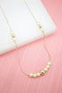 A delicate gold chain necklace features alternating pearls and gold beads resting against a soft pink backdrop.