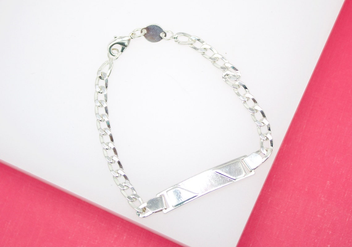 A polished silver ID bracelet rests against a pink and white background.