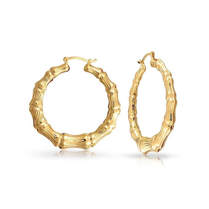 A pair of shiny gold bamboo hoop earrings rests against a white background.
