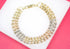 A tri-color gold multi-strand link bracelet featuring textured beaded details rests on a white display against a pink background.