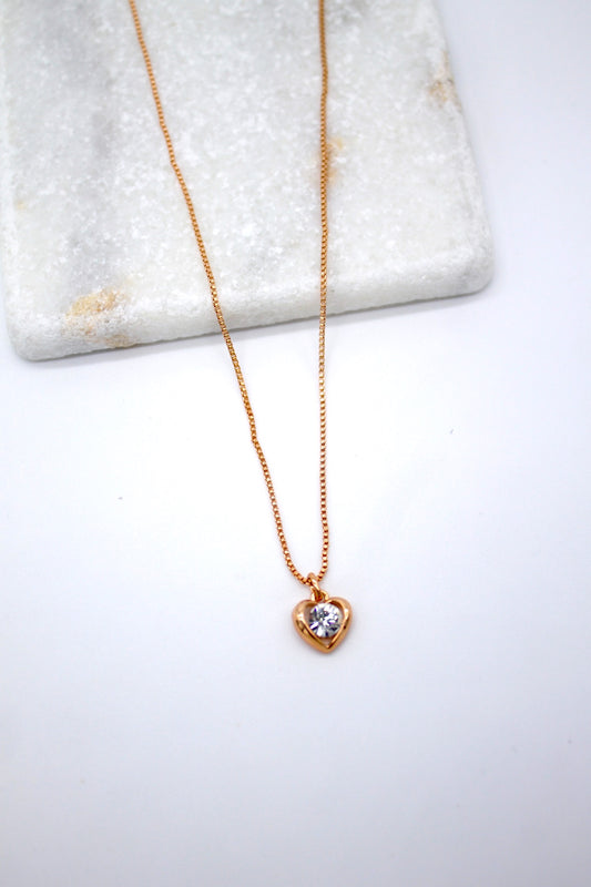 A delicate gold heart pendant necklace featuring a sparkling diamond accent rests elegantly against a white marble display.