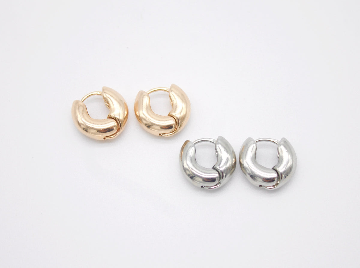 Two pairs of chunky huggie hoop earrings, one in gold and one in silver, rest side by side on a plain white surface.