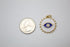 A round, gold-rimmed evil eye pendant with blue and white enamel rests beside a US quarter for scale.