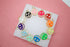 A colorful assortment of enamel smiley face charms with gold trim rests on a white display against a pink background.