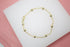 A delicate gold link bracelet adorned with evenly spaced round bead stations rests on a white display surface.