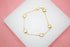 A delicate gold chain bracelet features sparkling square white crystal charms arranged against a white and pink background.