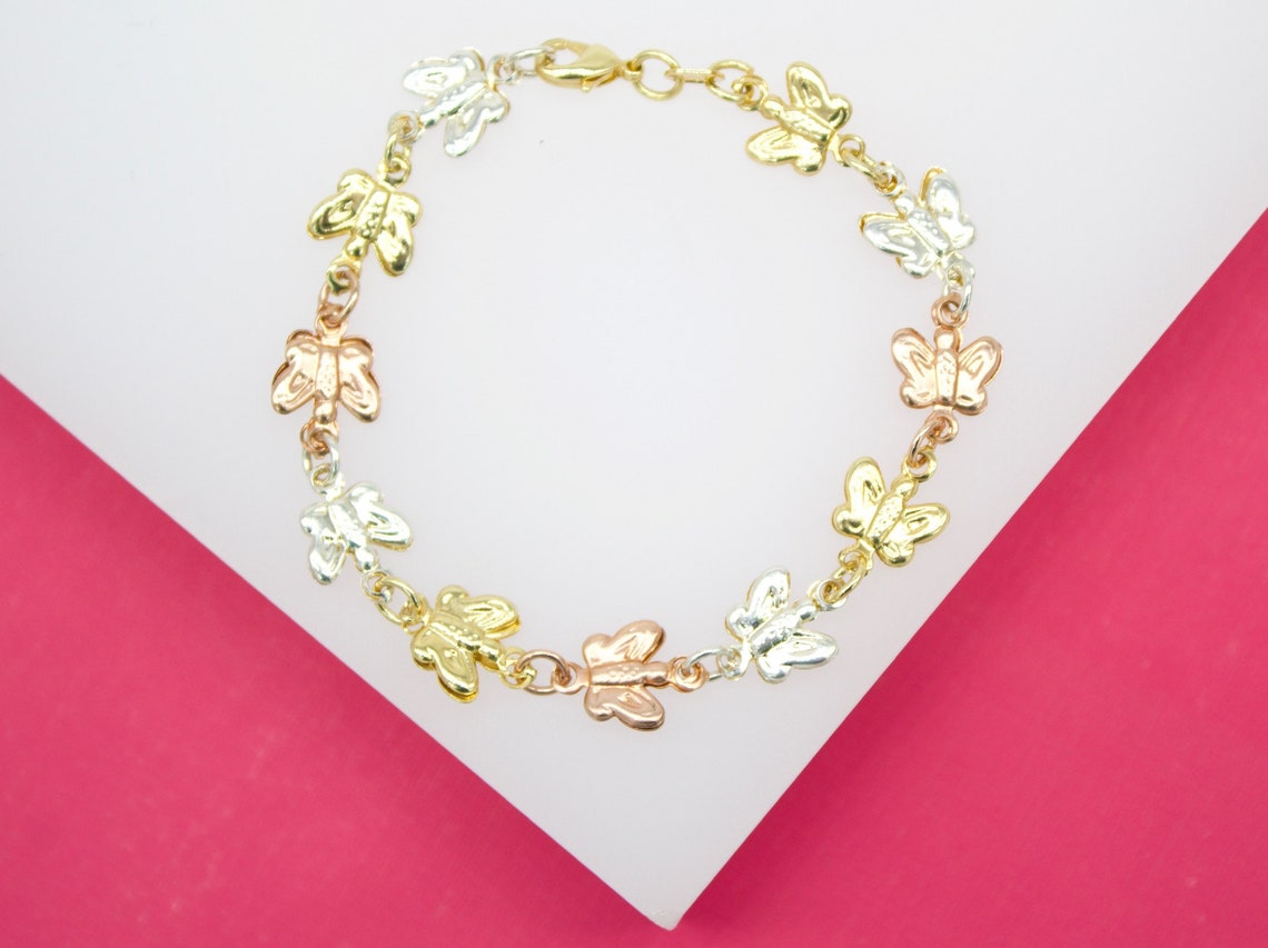 A delicate tri-color gold butterfly link bracelet rests on a white and pink display surface.