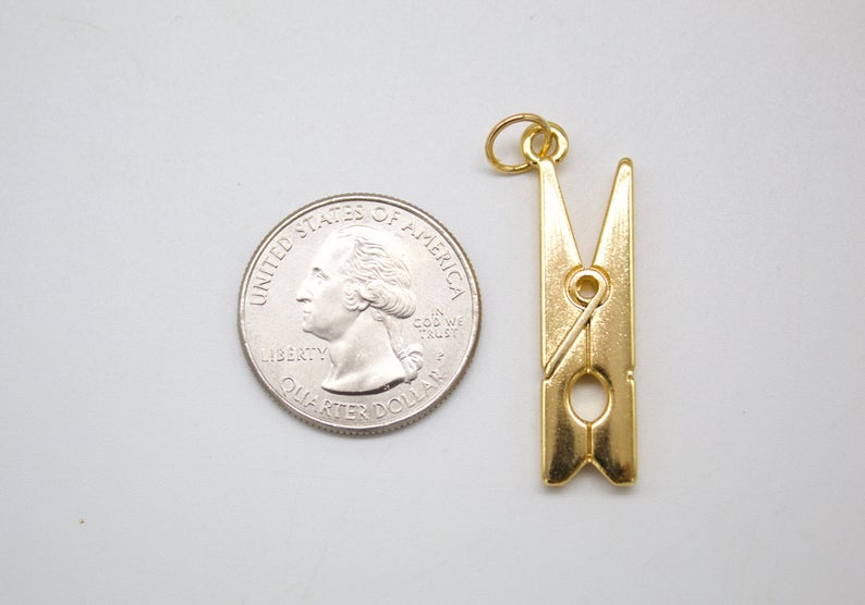 A shiny gold clothespin charm rests next to a US quarter coin to show its scale.