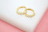 A pair of sparkling gold hoop earrings with small square zirconia stones rests on a white and pink surface.