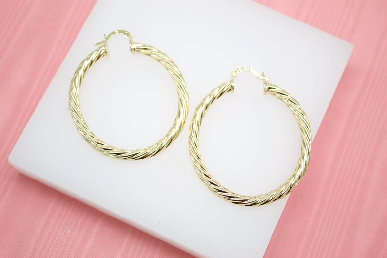 Two polished gold twisted hoop earrings rest side by side on a white display surface.