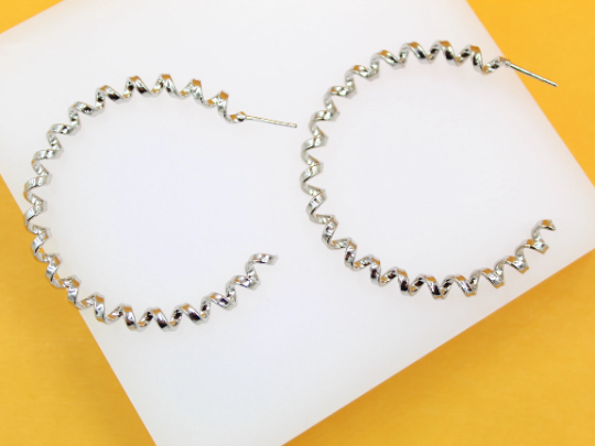 A pair of shiny silver spiral hoop earrings rests on a white display against a vibrant yellow background.