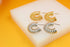Two pairs of spiral-shaped gold and silver hoop earrings rest neatly on a white display block against a vibrant yellow background.