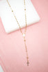 A delicate gold rosary necklace featuring shiny spherical beads rests against a white block on a soft pink background.