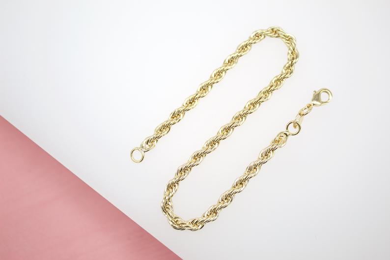 A gleaming gold rope chain bracelet lies gracefully on a light surface, showcasing its twisted link design and secure lobster clasp.