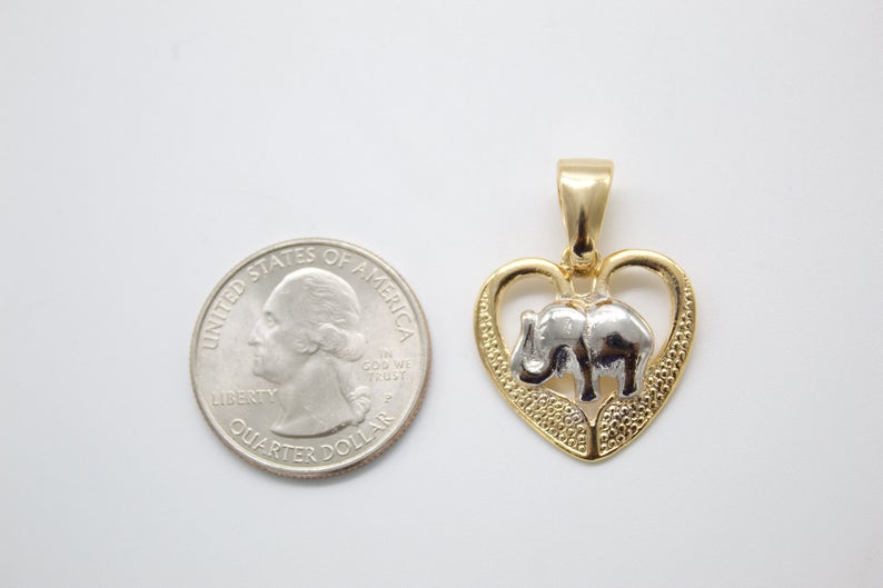 A two-tone gold and silver heart elephant pendant rests next to a US quarter coin for scale on a white surface.