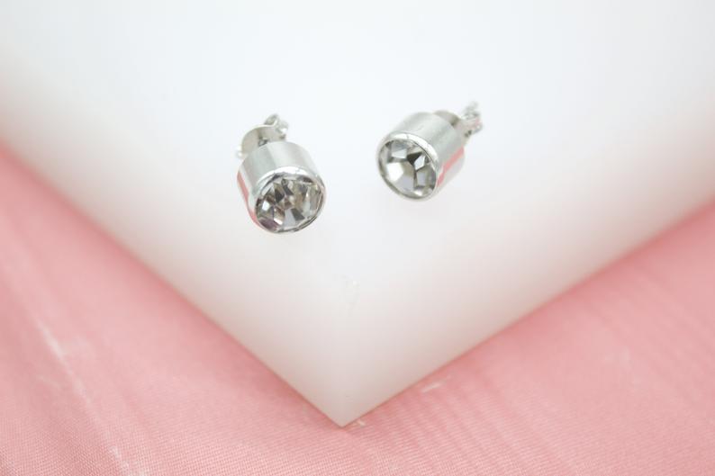 A pair of sparkling crystal stud earrings rests elegantly on a white and pink display surface.