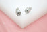A pair of sparkling crystal stud earrings rests elegantly on a white and pink display surface.