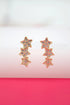 A pair of gold star crawler earrings featuring sparkling pink crystal-encrusted designs rests on a bright pink surface.