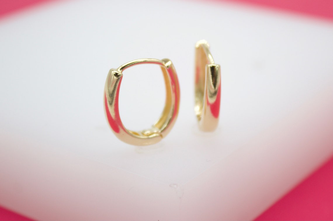 A pair of polished gold huggie hoop earrings rests on a white display surface.
