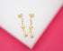 Two delicate gold star drop earrings rest on a white surface against a vibrant pink background.