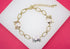 A gold-plated chain bracelet featuring three elephant charms with cutout hearts lies on a white display surface against a vibrant pink background.