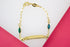 A gold ID bracelet features a link chain adorned with a green and a blue glitter diamond-shaped charm.