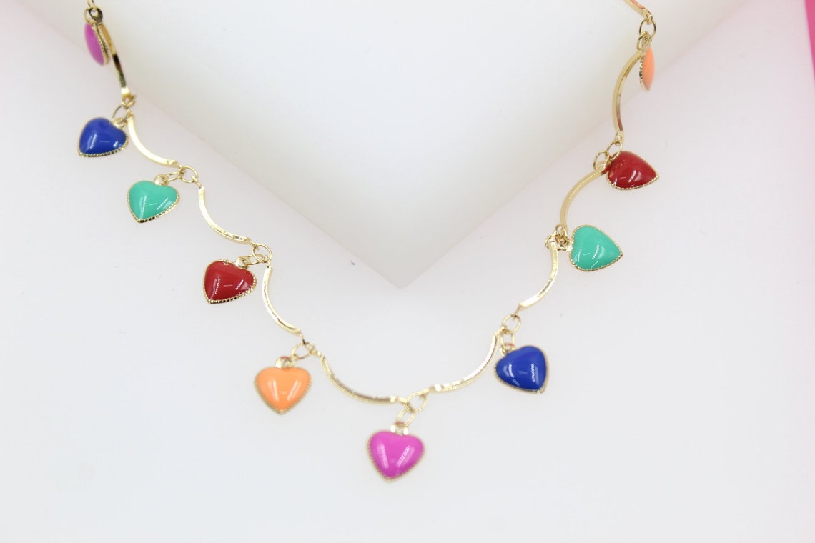A gold chain necklace displays colorful enamel heart charms in shades of red, blue, green, orange, and pink against a white background.