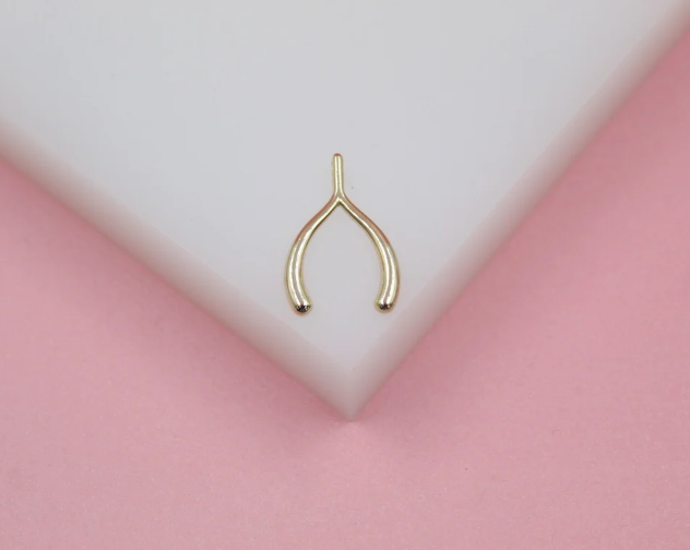 A delicate gold wishbone charm rests centrally on a white geometric block against a soft pink background.