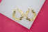 Two gold twist hoop earrings rest on a white surface against a bright pink background.