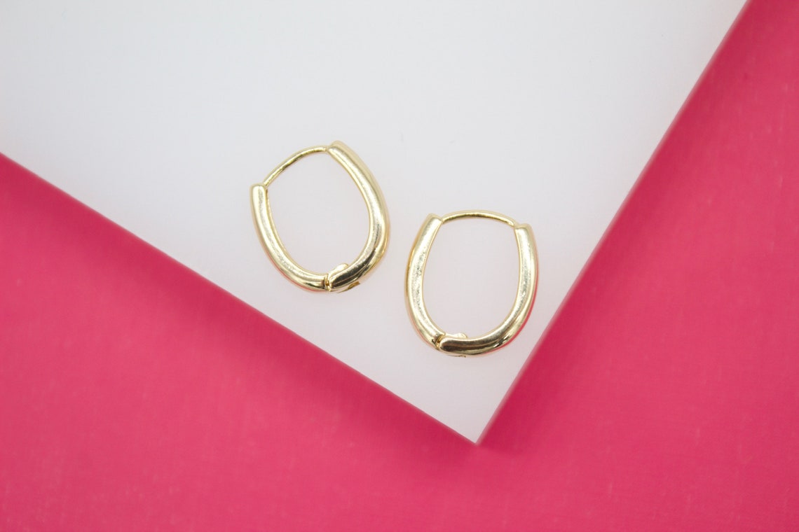 A pair of polished gold huggie hoop earrings rests on a white and pink display surface.
