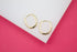 A pair of polished gold huggie hoop earrings rests on a white and pink display surface.