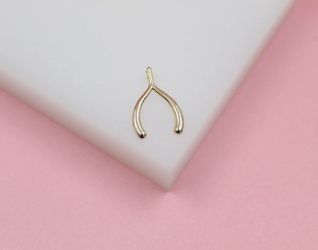 A small gold wishbone charm rests on a white and pink surface.