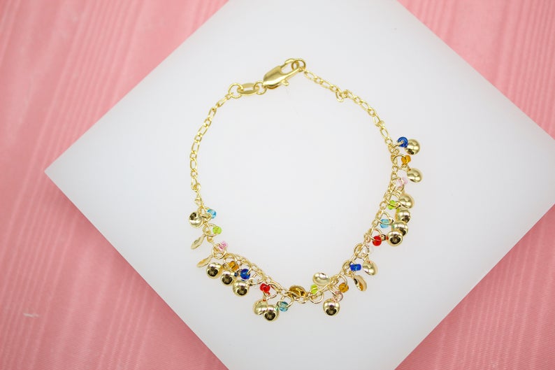 A delicate gold charm bracelet featuring tiny colorful beads rests on a white display surface.