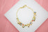 A delicate gold charm bracelet featuring tiny colorful beads rests on a white display surface.