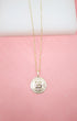 A delicate gold chain holds a textured Bitcoin coin pendant against a soft pink background.